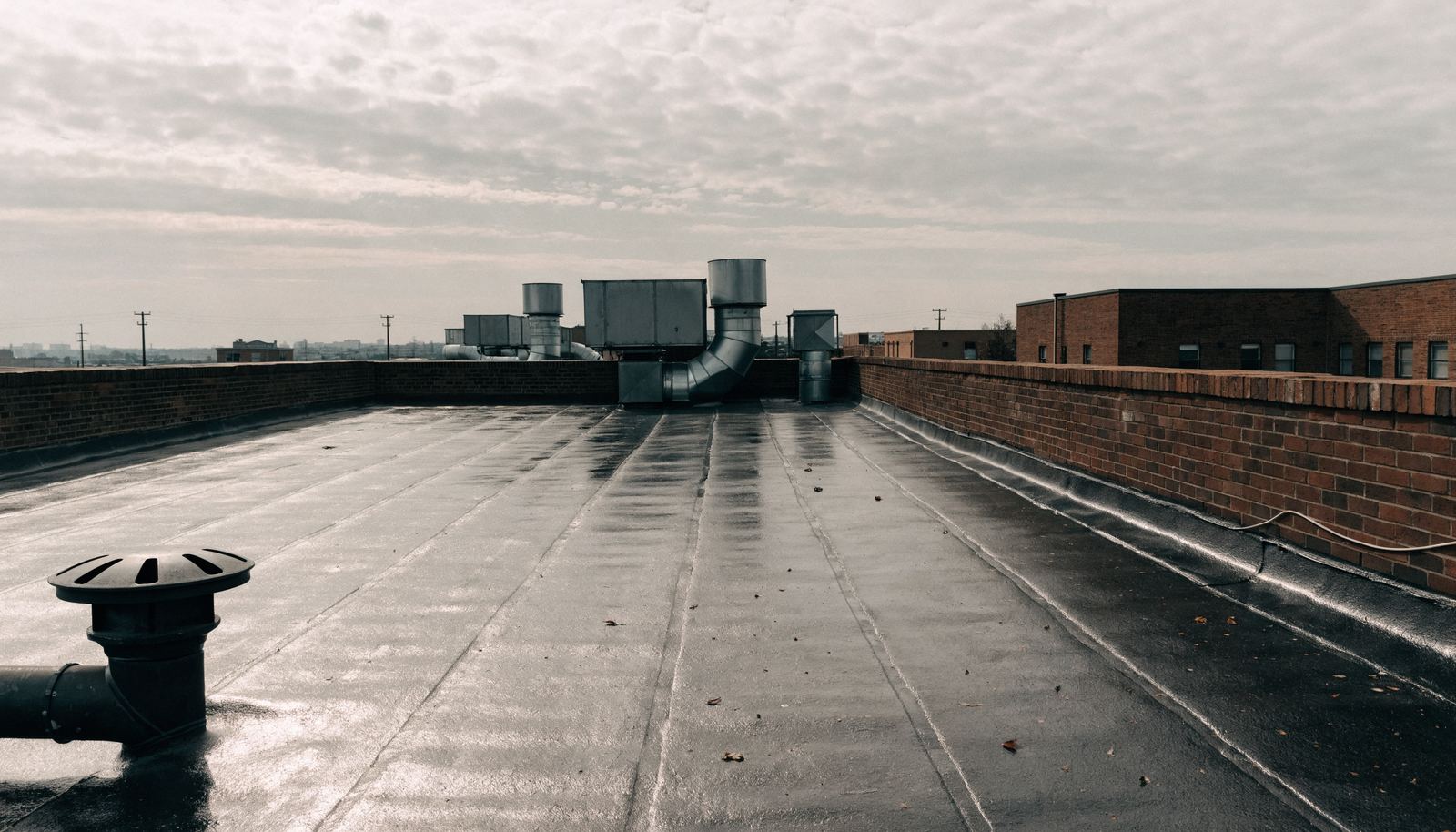A flat commercial roof in Hamilton with membrane seams, a brick parapet wall and a roof drain